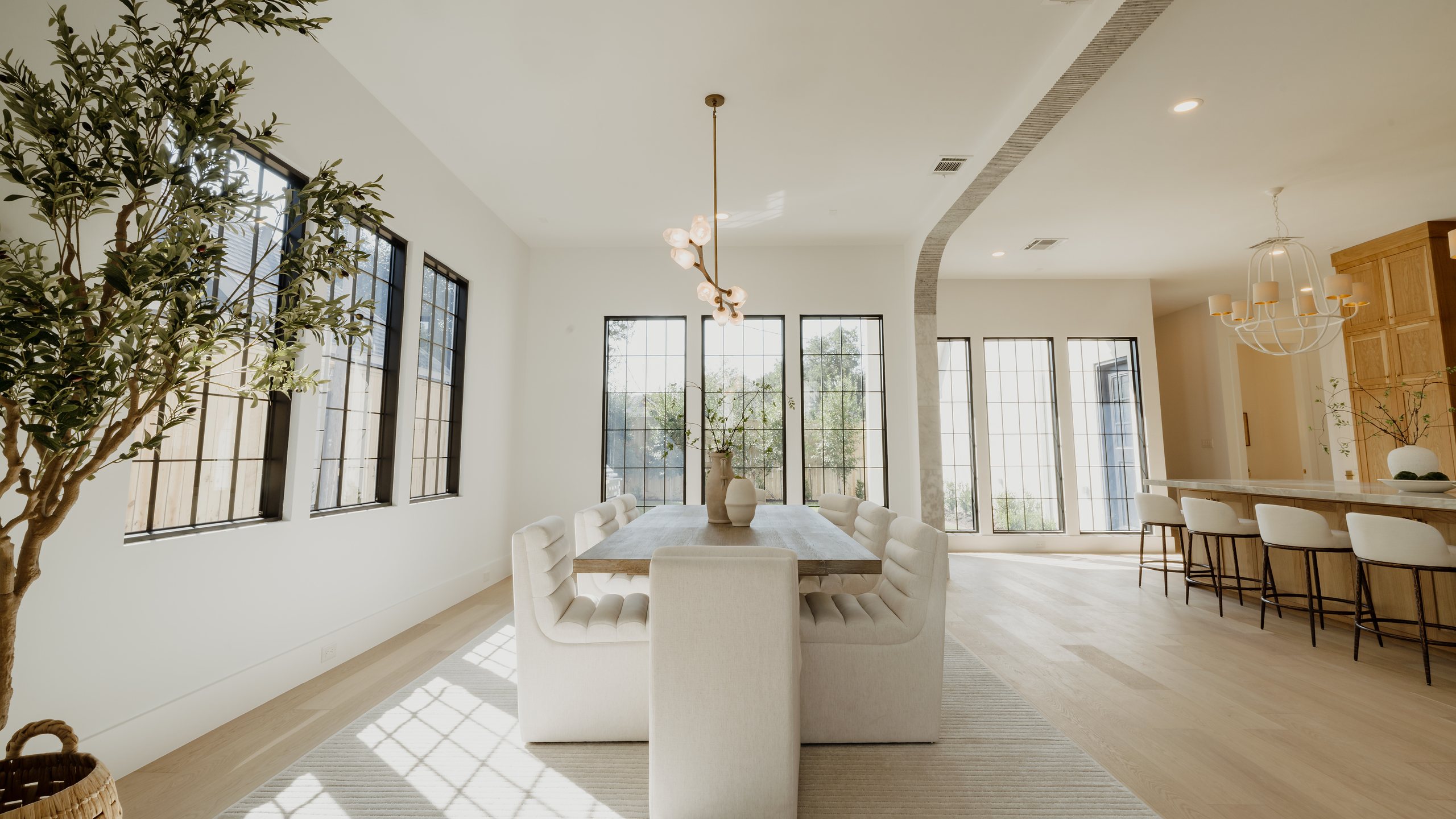 Dining room with a long table, upholstered chairs and black steel windows at R+R Garden Oaks