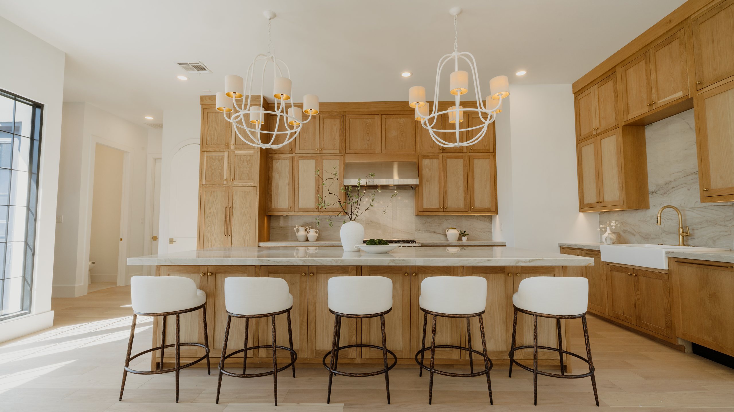 White oak kitchen with a large island, five counter stools and white chandeliers