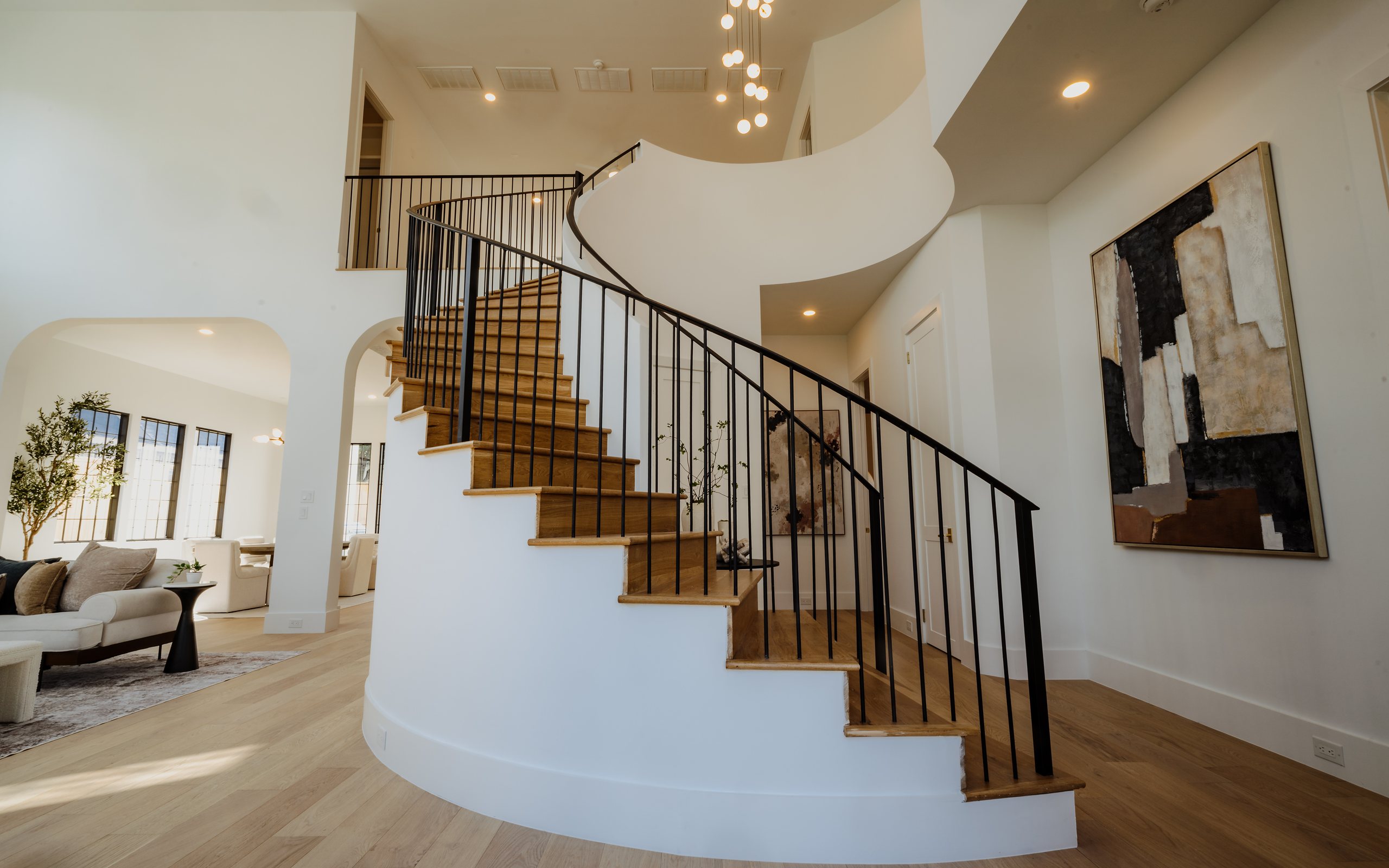 Curved oak staircase with a black iron railing rising from the living room